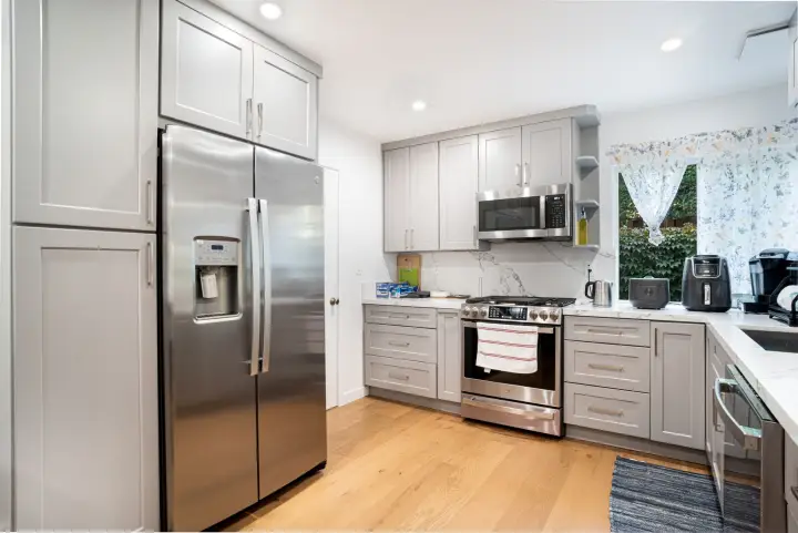 A bright kitchen with grey shaker cabinets, white stone counters, stainless appliances and oak floors.