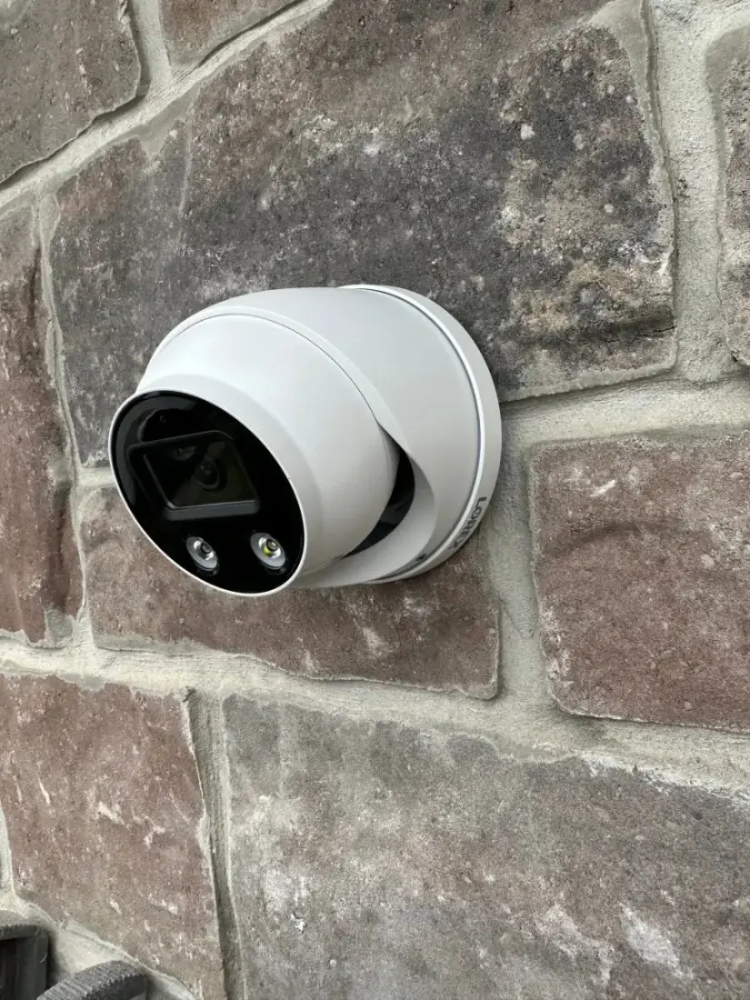 A white dome security camera installed on a stone exterior wall