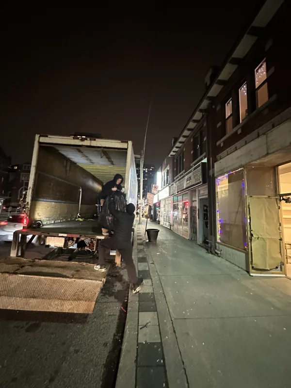 Crew members loading a moving truck outside a row of shops in the evening