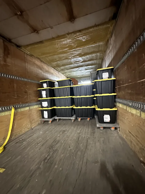 Black moving bins with yellow lids stacked inside the moving truck