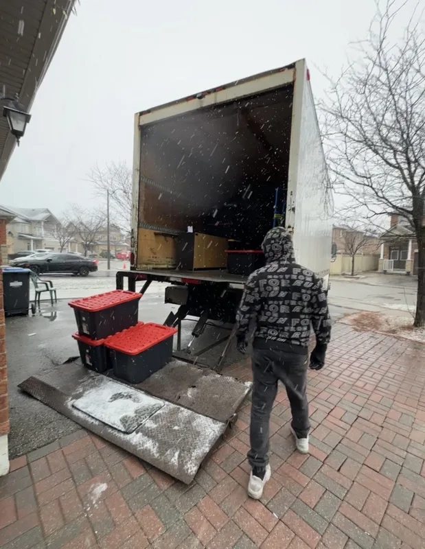 An Optimum crew member beside a moving truck and bins on a snowy driveway